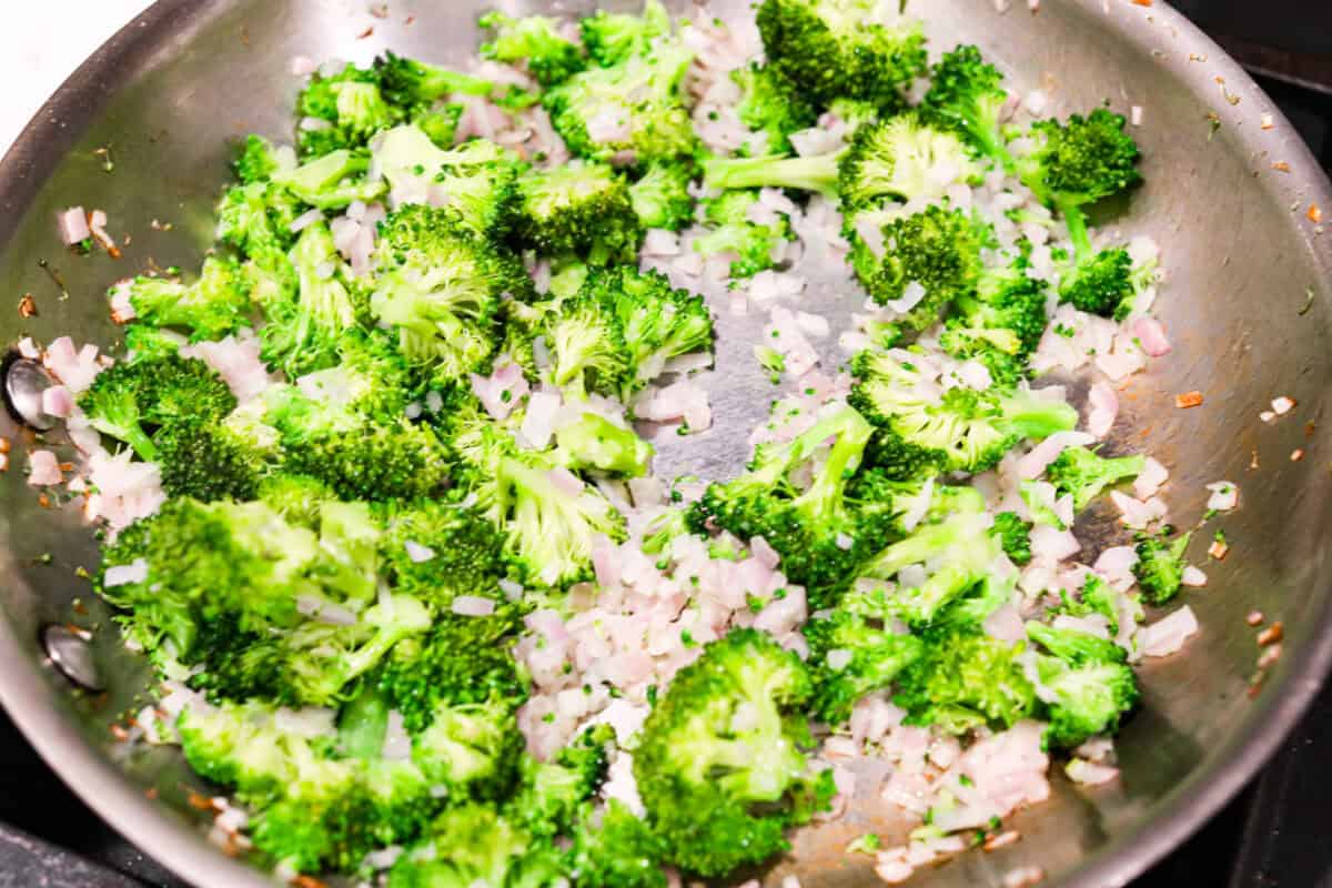 Overhead shot of shallots and broccoli cooking in a large skillet. 