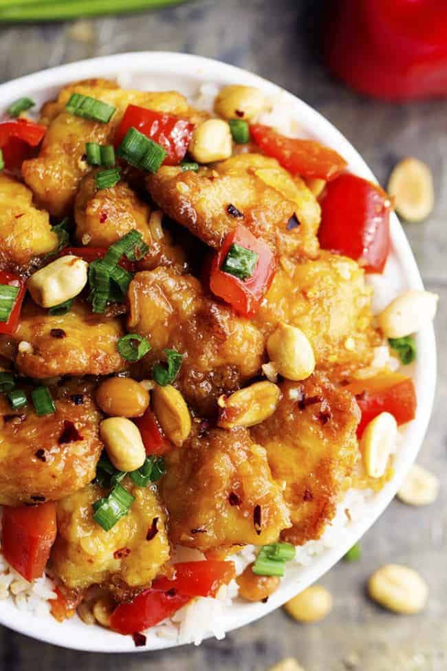 Baked Kung Pao chicken in a bowl with white rice and garnished with peanuts. 