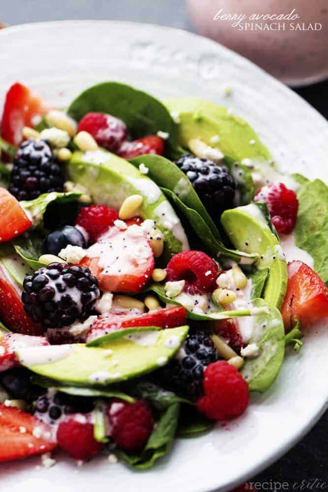 Berry avocado spinach salad on a white plate.