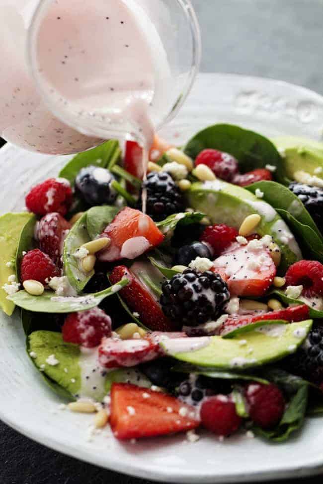 Pouring dressing on the fresh spinach berry salad.