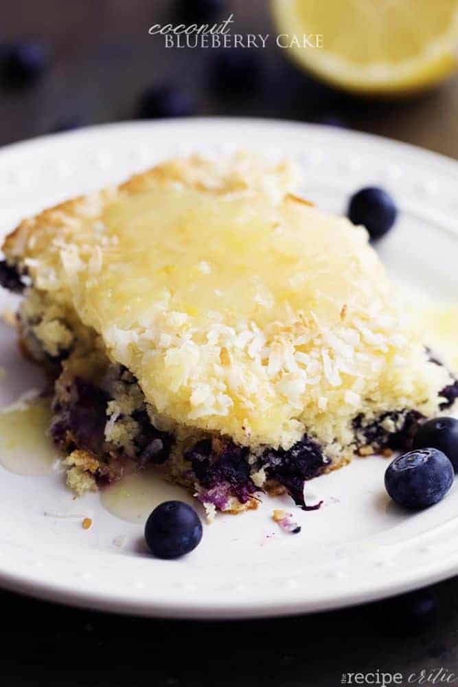 coconut blueberry cake serving on a white plate with blueberries for garnish.