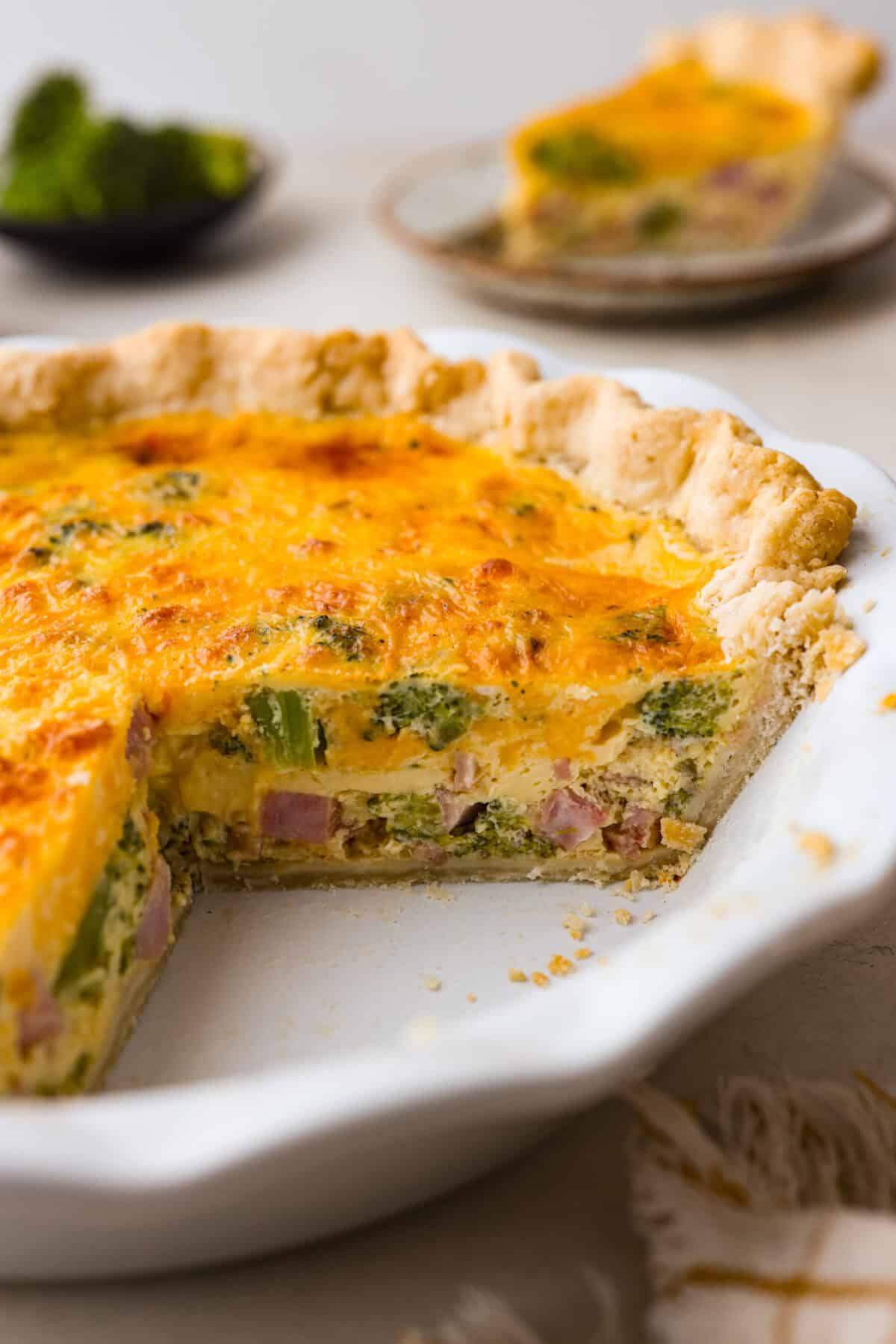 Side shot of ham and broccoli quiche with a slice taken out. 