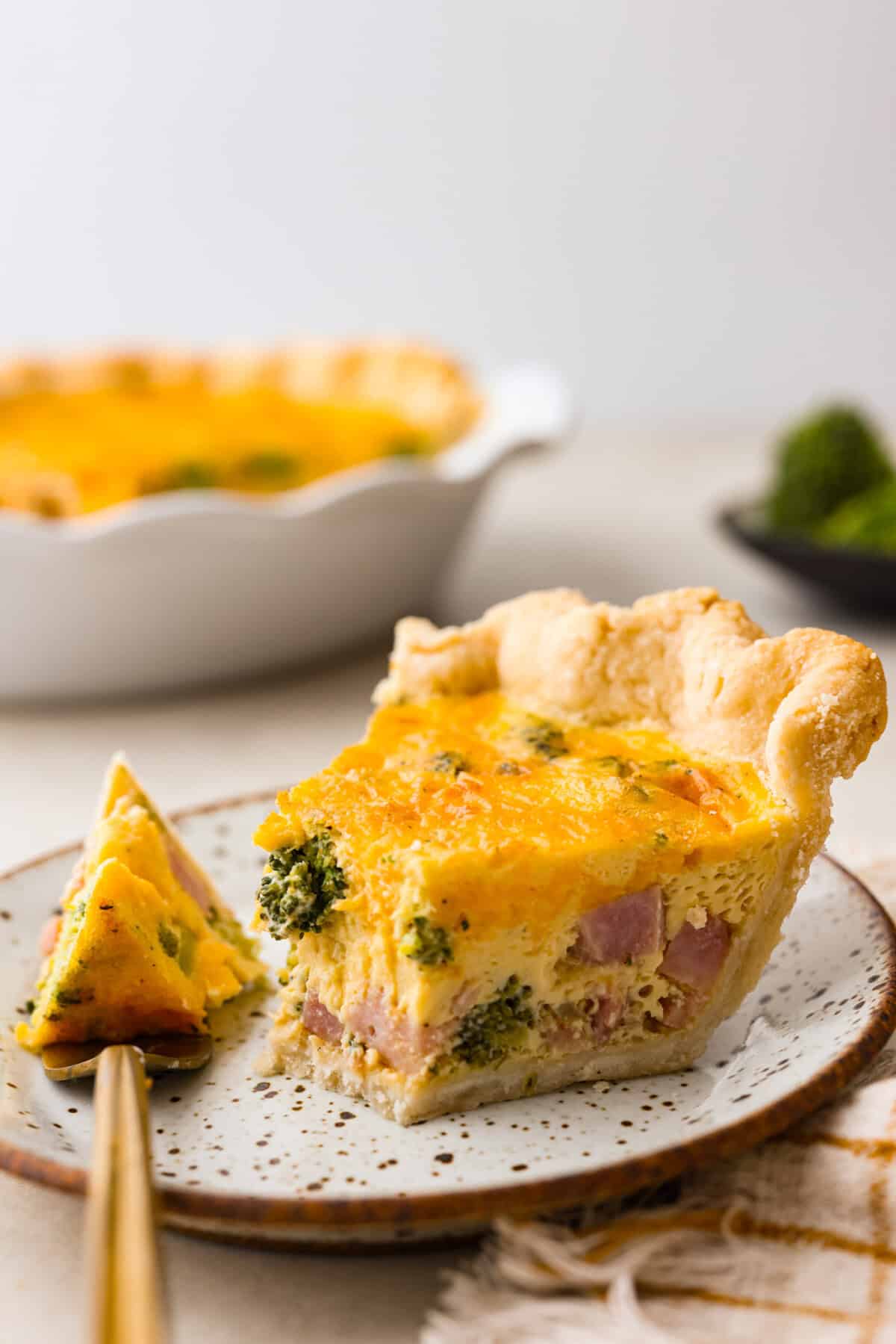 Close up shot of a plated slice of quiche with a bite on a gold fork.