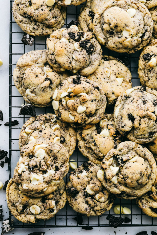 A bunch of white chocolate oreo cookies stacked over and on top of each other on a cooling rack.