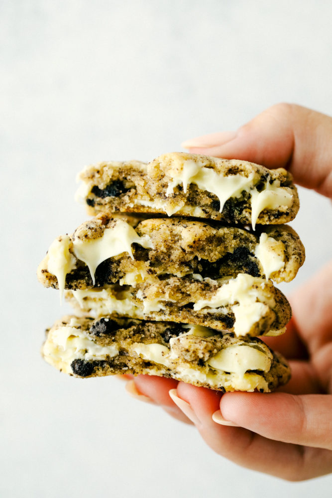 White chocolate oreo cookies stacked on top of each other and being held up with a hand. 