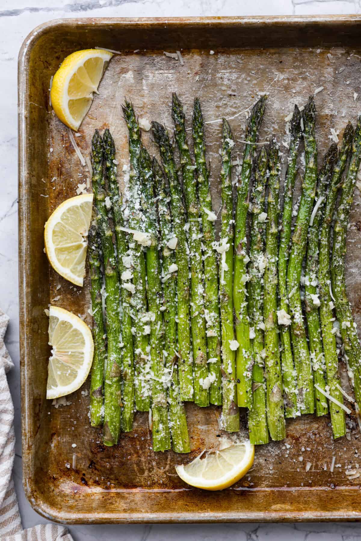 Top view of roasted lemon parmesan garlic asparagus on a sheet pan with lemons.