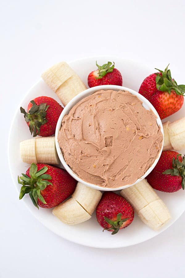 Peanut butter fruit dip in a white bowl with strawberries and bananas around it.