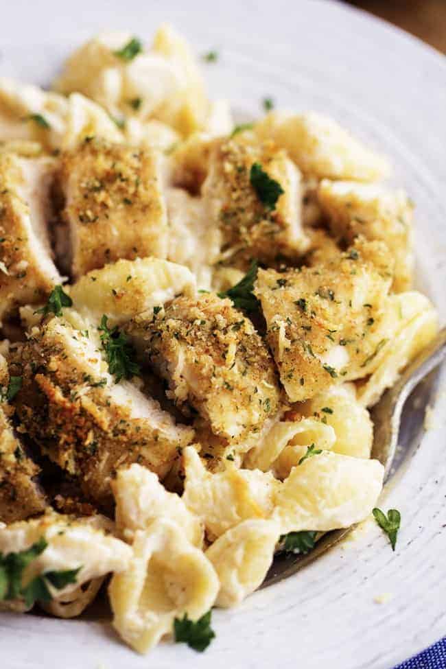 Scooping a spoonful of creamy garlic noodles and chicken out of a white bowl.