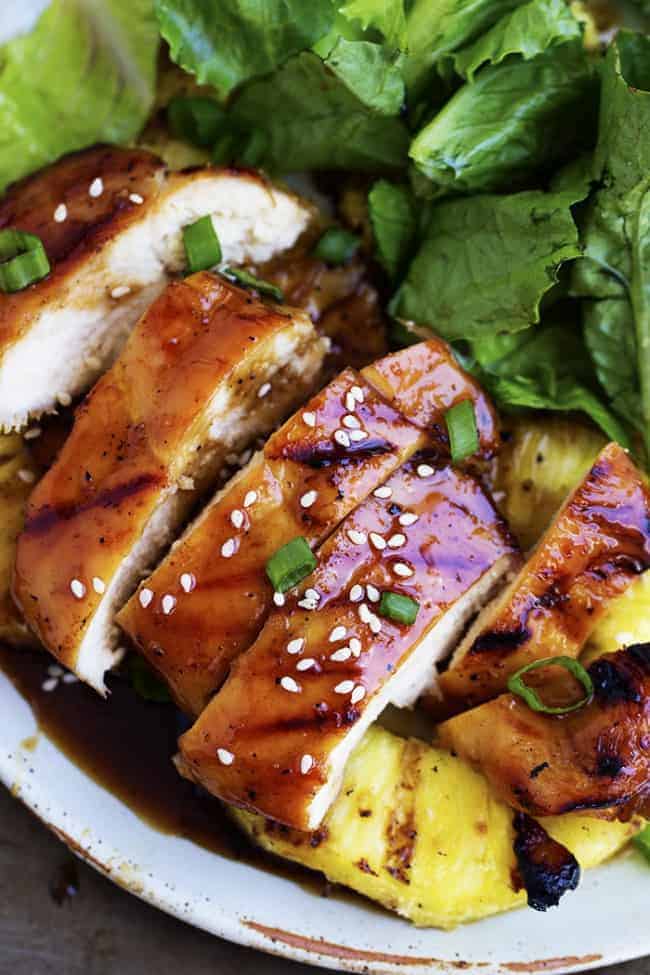 Grilled pineapple teriyaki chicken with salad and pineapple on a white plate.