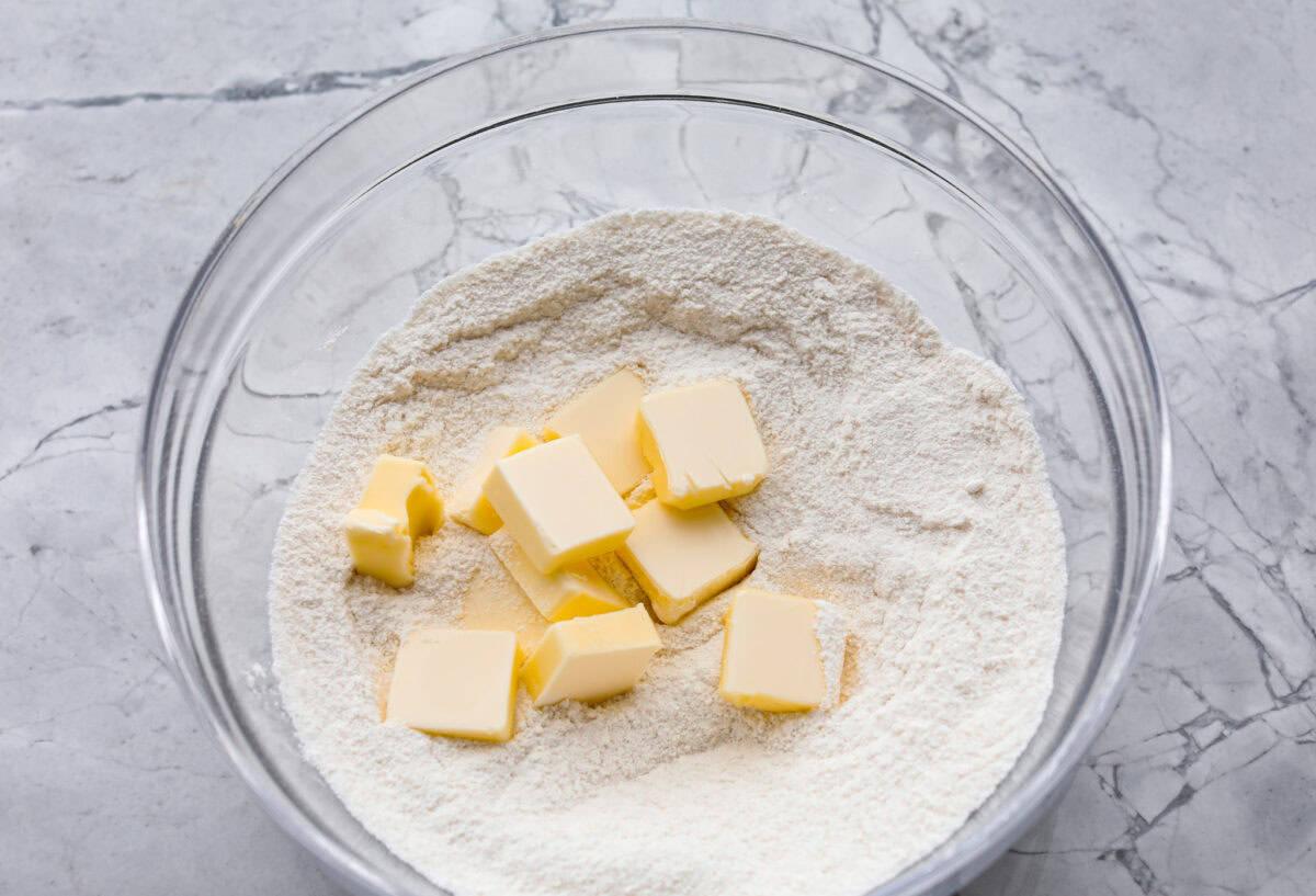 Overhead shot of dry ingredients mixed in a glass bowl with cubed butter on top. 