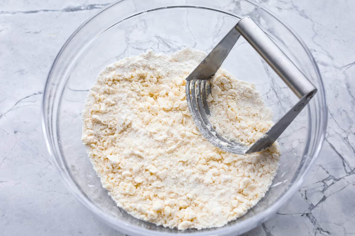 Overhead shot of dry ingredients mixed with butter with a pastry cutter. 