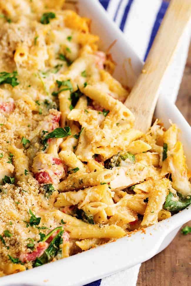 pesto alfredo chicken casserole in a white baking dish with a wooden spoon.