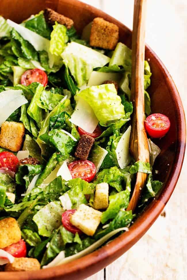 classic caesar salad in a red bowl with wooden spoon.