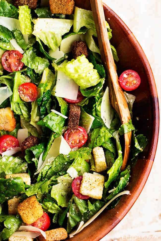 classic caesar salad areal view in a red bowl with wooden spoon.