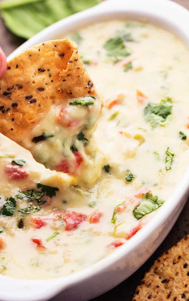 White Spinach Queso in a white dish with a tortilla chip dipping into it.