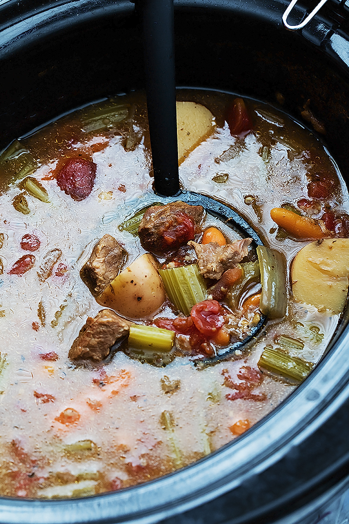 Beef stew in a black crock pot with a black ladle.