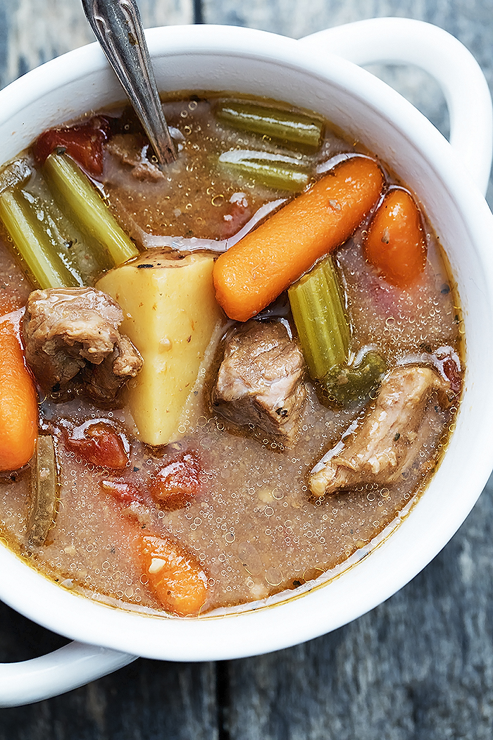 Areal view of beef stew in a white bowl with a spoon in it.