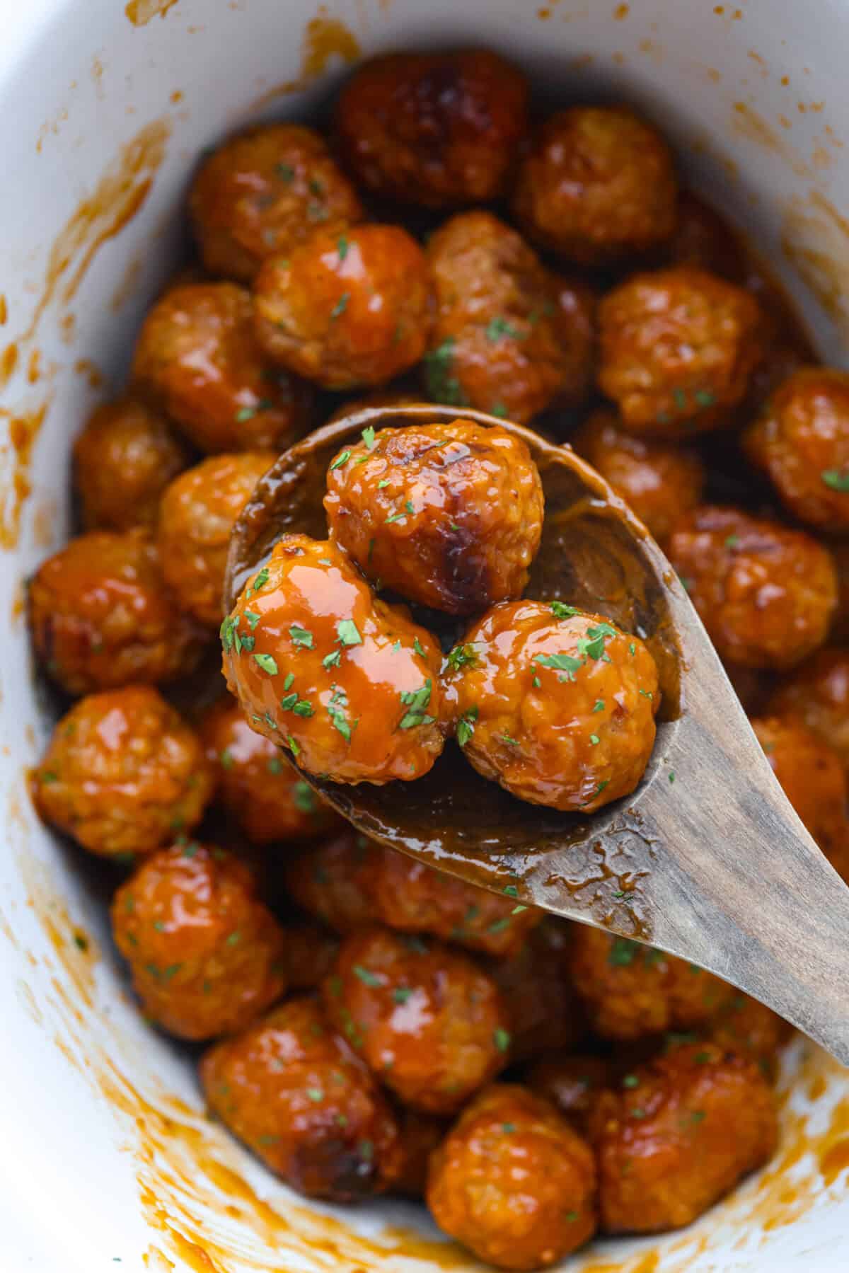 Overhead shot of slow cooker honey buffalo meatballs with wooden spoon and three meatballs on it. 