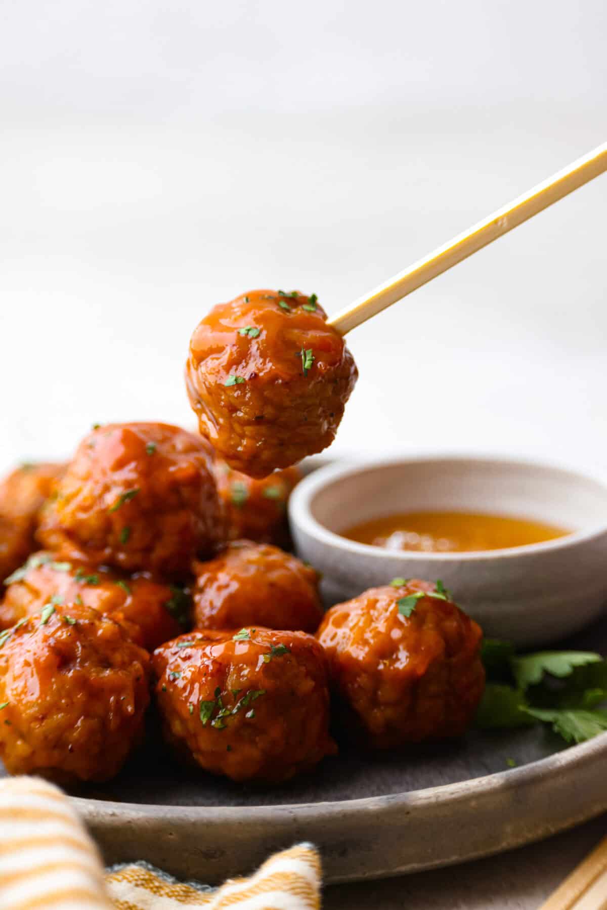 Side shot of plated slow cooker honey buffalo meatballs with one on a skewer. 