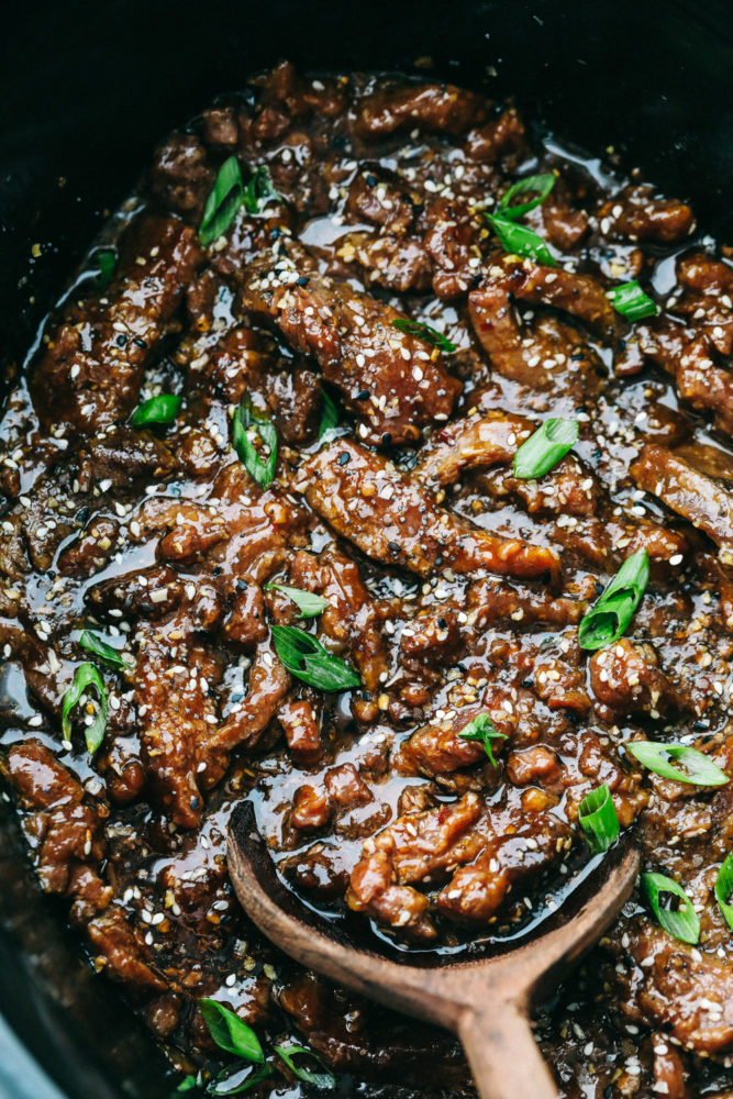 Korean beef meat in the slow cooker being stirred with a wooden spoon. 