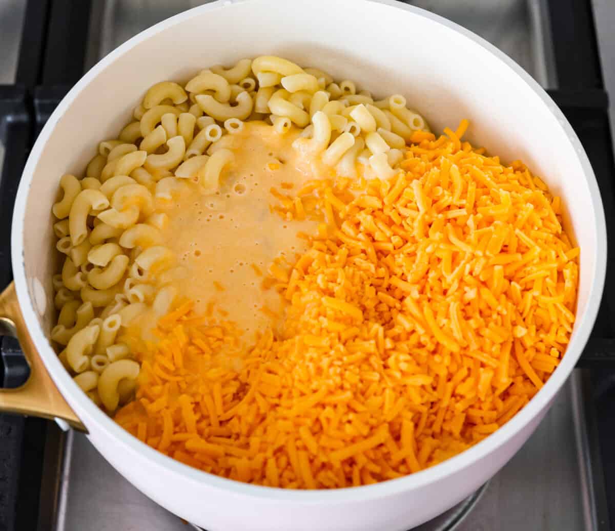 Overhead shot of cooked pasta, squash puree and cheese in a pot on the stovetop. 