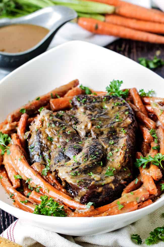 Roast and carrots in a white serving bowl.