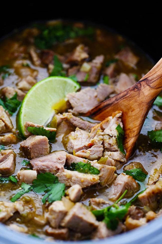 Close up photo a pork Chile Verde with a wooden spoon and a fresh cut lime on top.