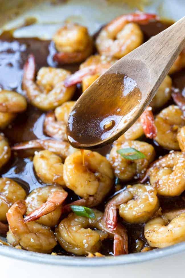 Teriyaki shrimp in a skillet with a wooden spoon.