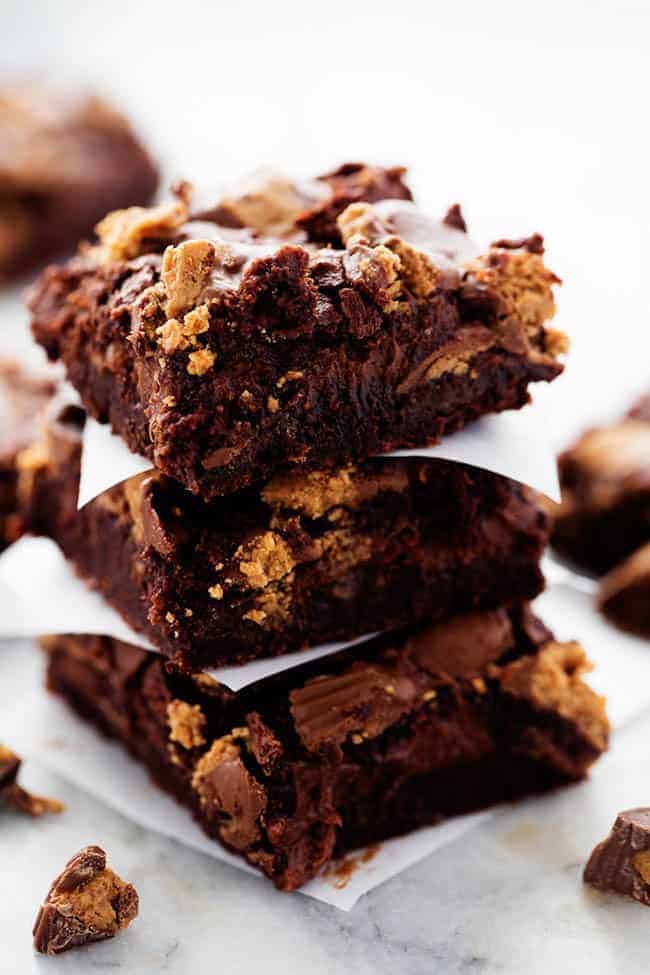 Hot Fudge Peanut Butter Cup Cheesecake Brownies stacked on top of one another with parchment paper in between them.