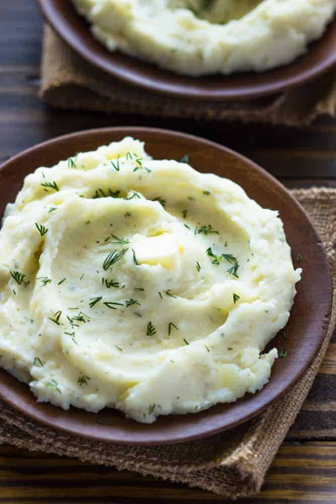 Slow Cooker Ranch Mashed Potatoes on a brown bowl on a wood table. There is a brown cloth under the bowl. 