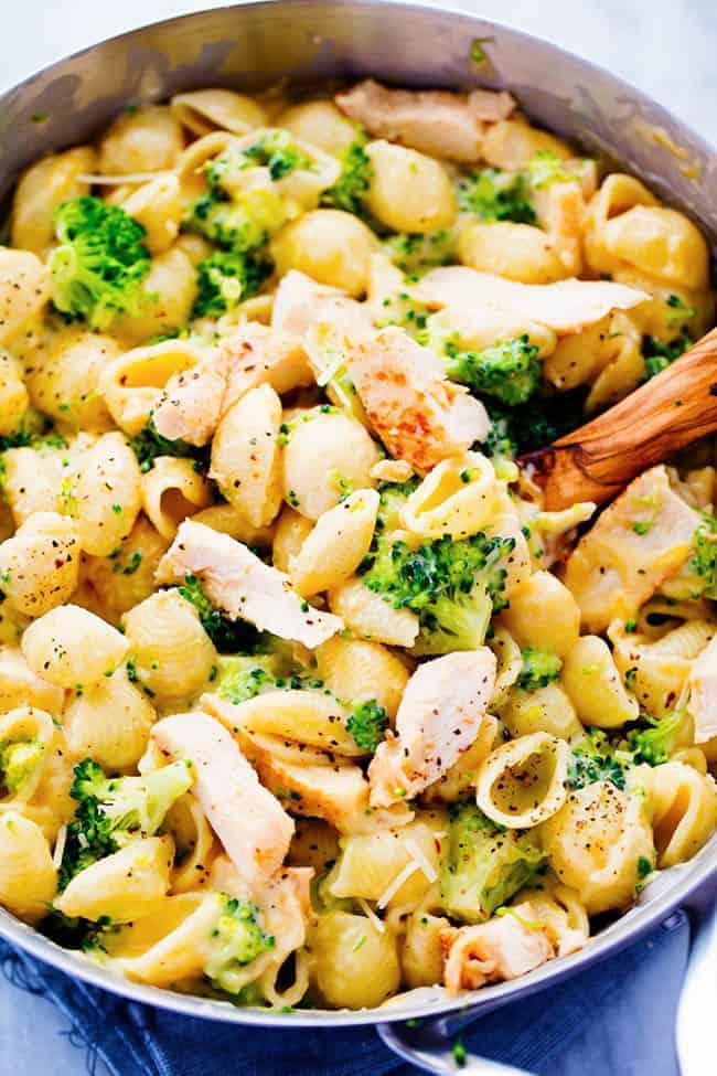 CHEESY CHICKEN BROCCOLI SHELLS IN A PAN WITH A WOODEN SPOON.  