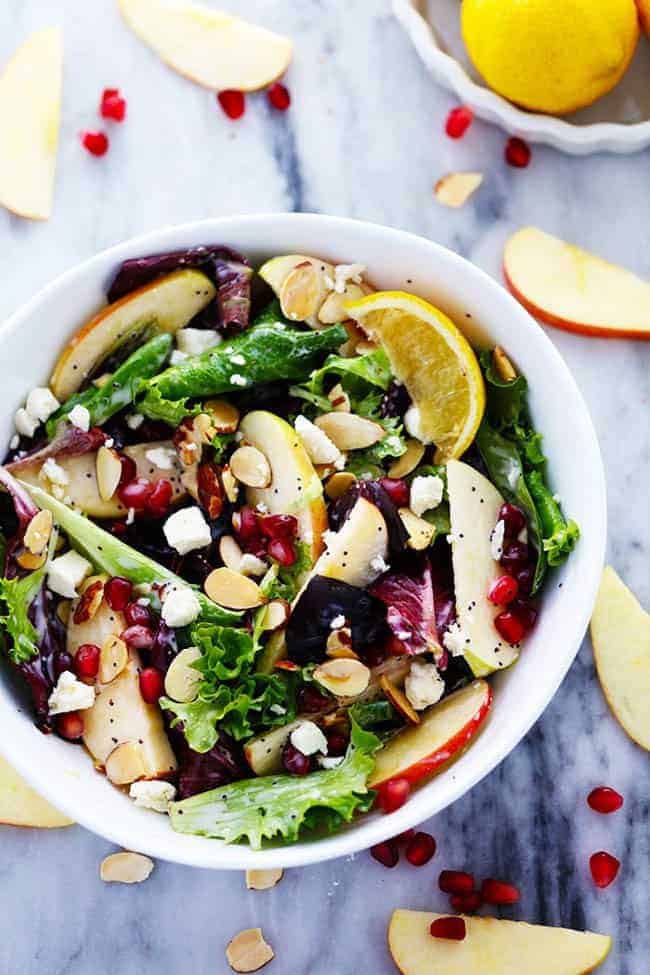 Apple Pomegranate Almond Salad with a Creamy Lemon Poppyseed Dressing in a white bowl with fresh cut apples on the side. 