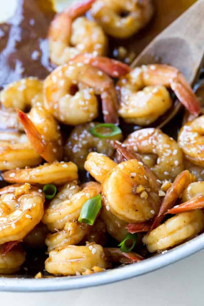 Teriyaki shrimp in a skillet with a wooden spoon.