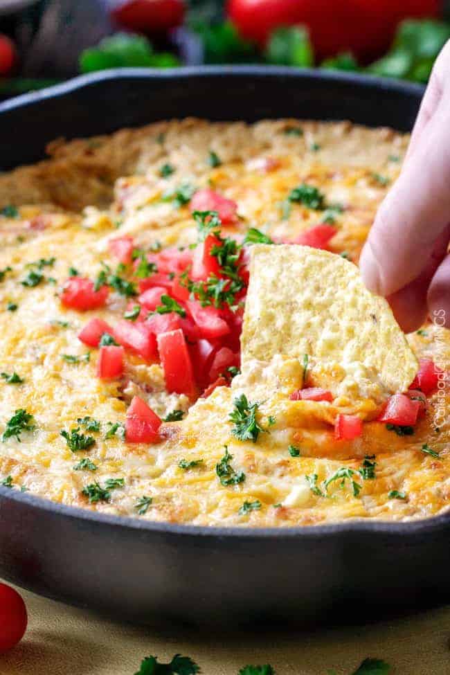 Queso verde corn dip in a large skillet with a chip being dipped into it. 