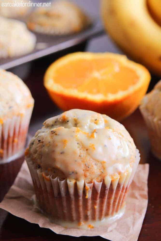 Banana Poppy Seed Muffins with an Orange Glaze with a fresh sliced orange in the background. 