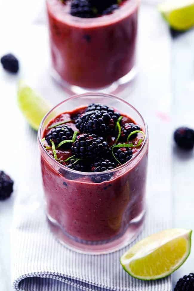 Blackberry lime smoothie in a clear glass with fresh cut limes on the side with fresh blackberries.s