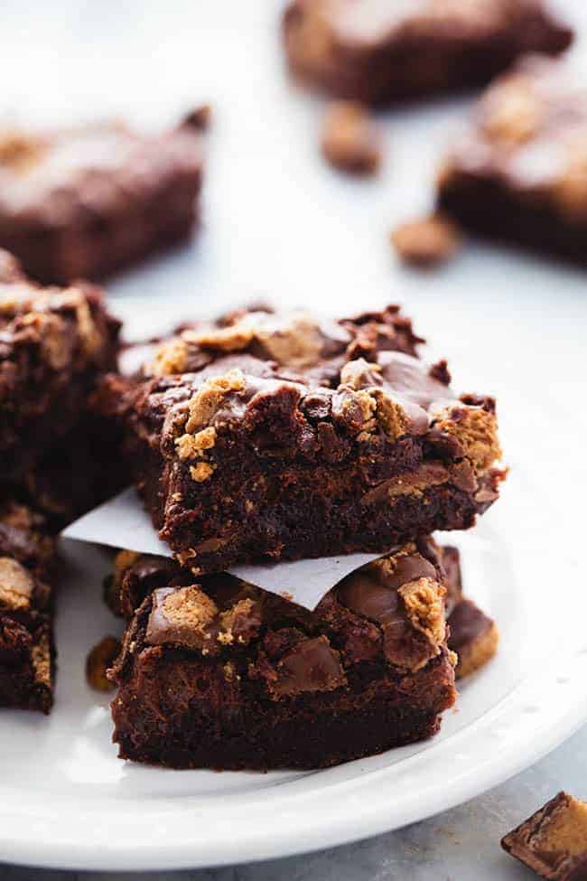 Hot Fudge Peanut Butter Cup Cheesecake Brownies stacked on top of one another on a white plate.