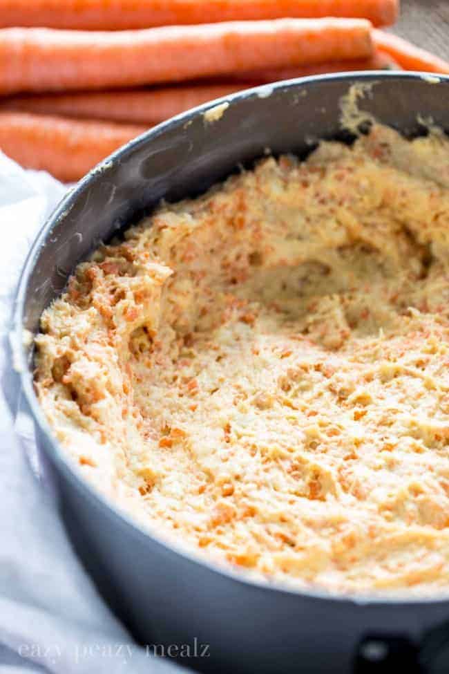 Carrot coffee cake batter in a mixing bowl with fresh carrots in the background.