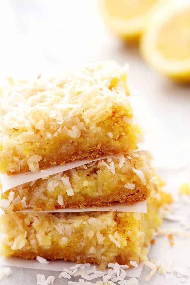 Lemon coconut butter bars stacked on top of each other with fresh cut lemons in the background.