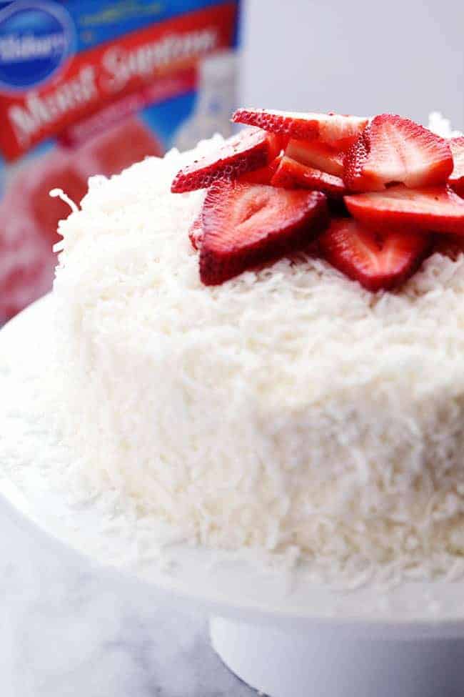 Strawberry Coconut Cream Cake with Coconut Cream Cheese Frosting with fresh cut strawberries on a white cake stand. 