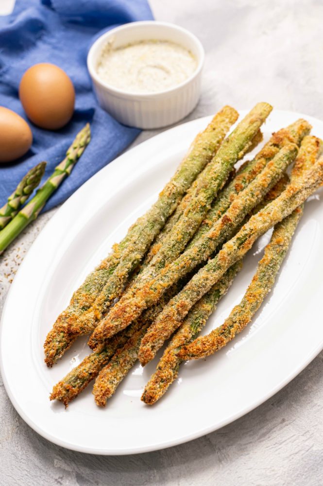 Parmesan Herb Asparagus Fries on a white plate with uncracked eggs on the side. 