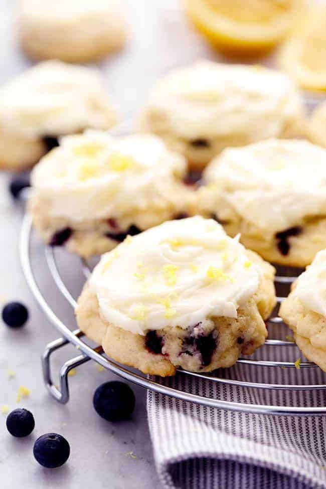 Blueberry Lemon Cookies with Lemon Cream Cheese Frosting on a cooling rack. There are some fresh blueberries under the cooling rack. 