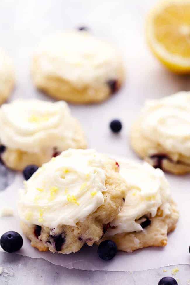 Blueberry Lemon Cookies with Lemon Cream Cheese Frosting on a white plate with cut lemon in the background. 