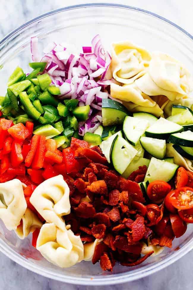 Ingredients in a clear bowl for Zesty Tortellini Bacon Vegetable Salad.