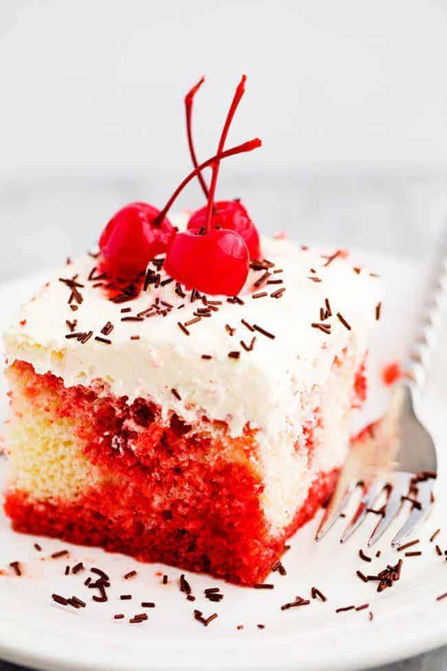 Cherry Jello Coke Poke Cake on a white plate with a metal fork with cherries on top. 