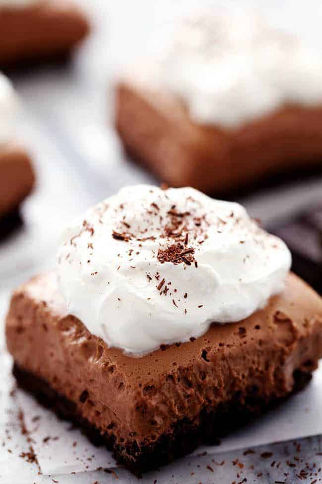 French Silk Pie Bars with whipped topping placed on white parchment paper. 