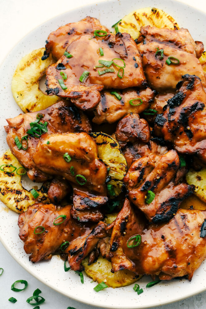 Grilled Huli Huli Chicken on a plate with grilled pineapple and garnished with green onions. 