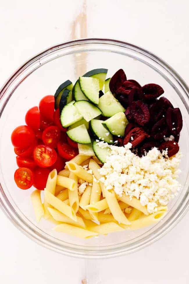 Greek Tzatziki Pasta Salad ingredients in a glass bowl. 