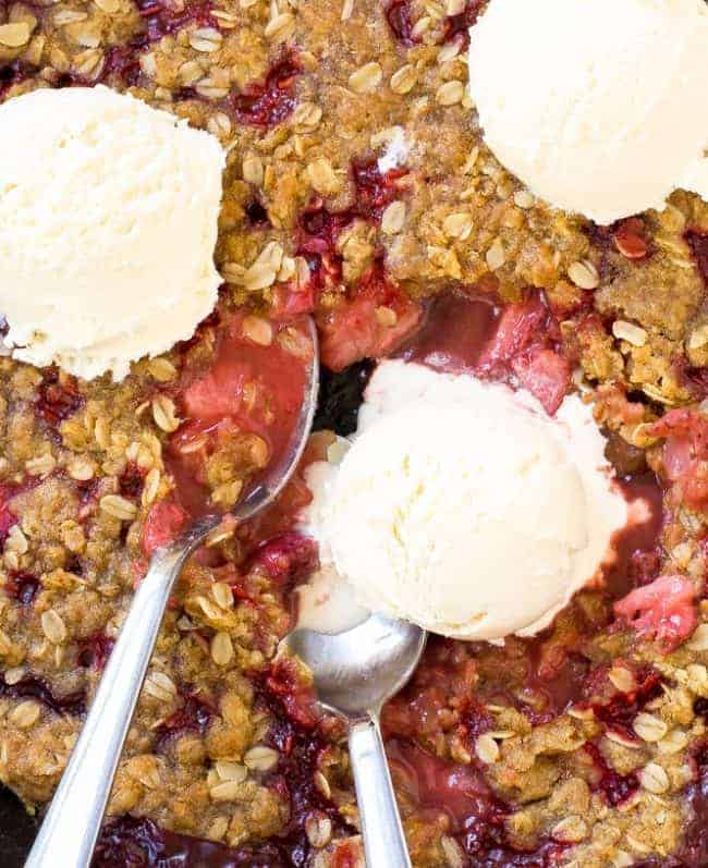 Strawberry Crisp with three scoops of ice cream on top with two metal spoons. 