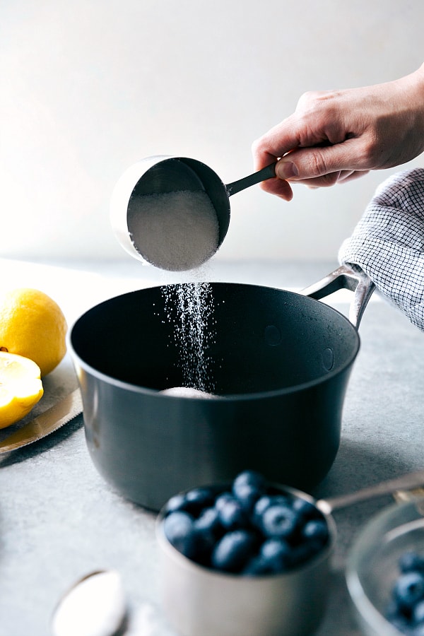 A cup of sugar being added to a pot. 